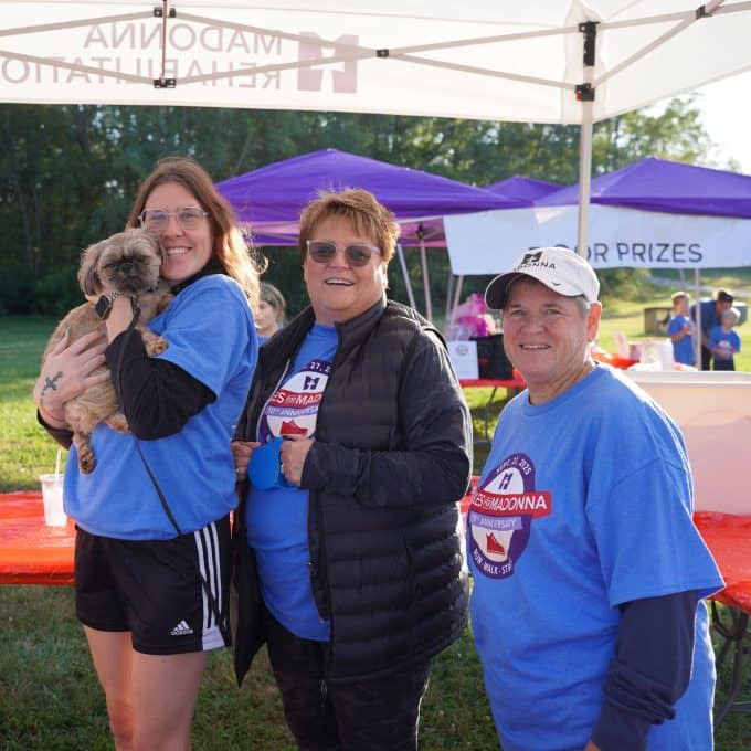3 women with Miles for Madonna t-shirts smile as one woman holds a small dog