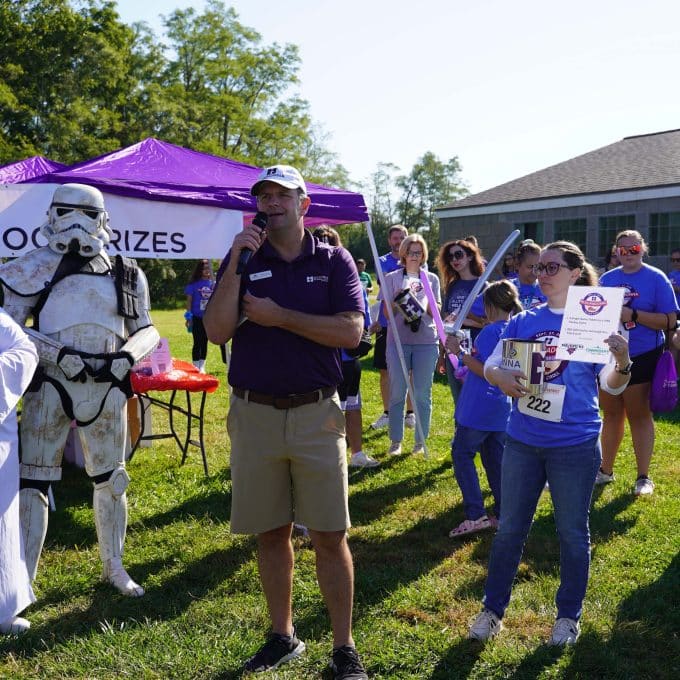 Race announcer holds microphone up while speaking to a crowd of attendees