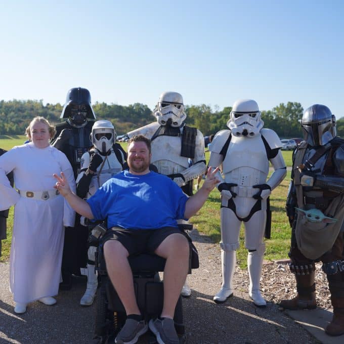 Man in wheelchair poses in picture with several character cosplayers from Star Wars