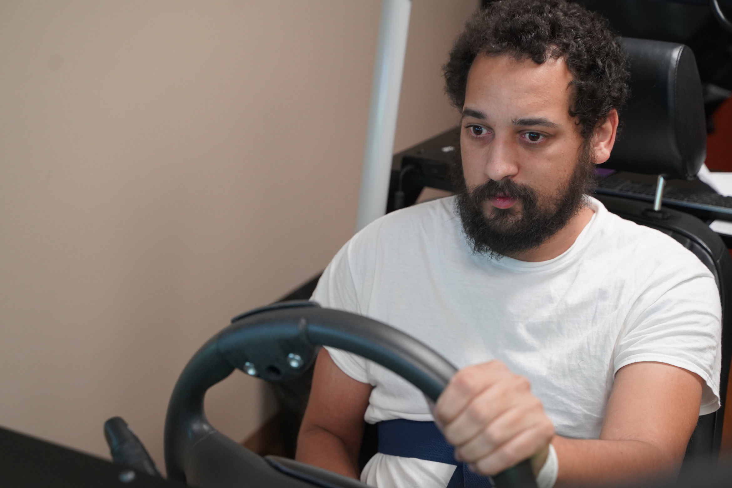 A bearded man sits at the wheel of a driving simulator at Madonna Rehabilitation Hospitals